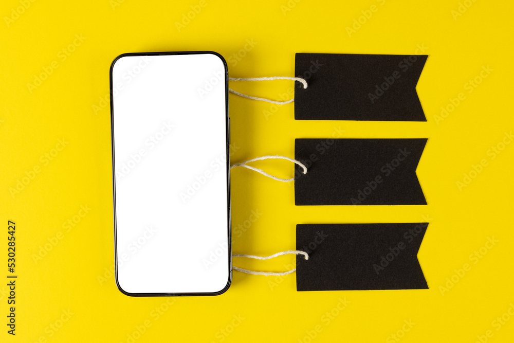 Composition of smartphone with gift tags on yellow background