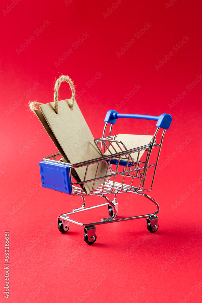 Composition of shopping cart with bag and copy space on pink background