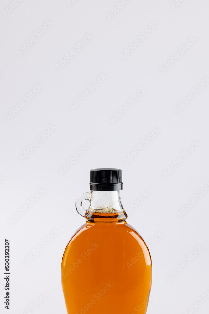 Vertical image of glass bottle of maple syrup on white background, with copy space