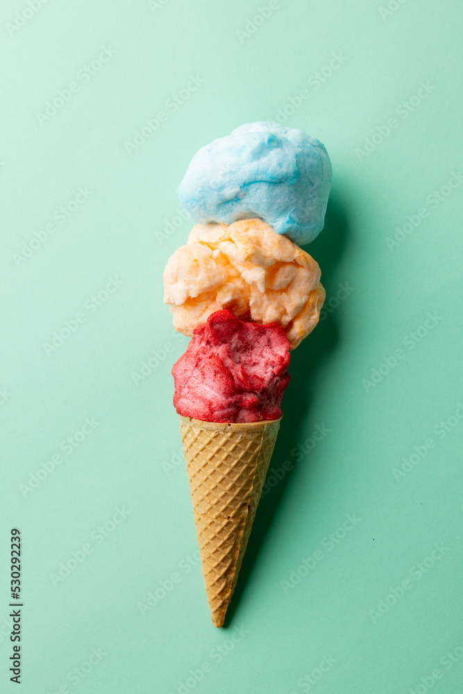 Vertical image of three coloured flavours of ice cream in cone, on blue background with copy space