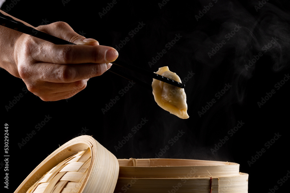 Overhead view of asian dumpling held in black chopsticks by caucasian man on black background