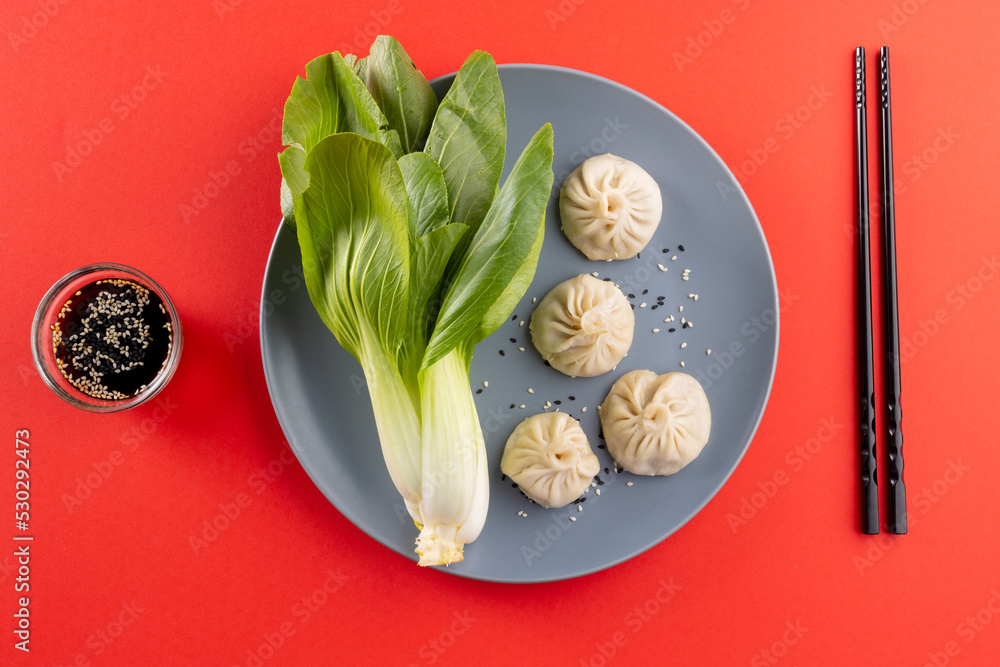 Overhead view of asian dumplings, soy sauce, endive and chopsticks on red background