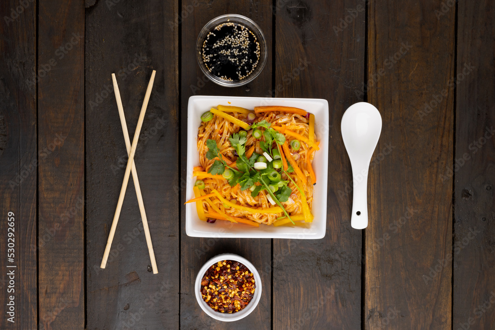 Overhead view of asian wok stir fry noodles and chopsticks, spoon and condiments on wood