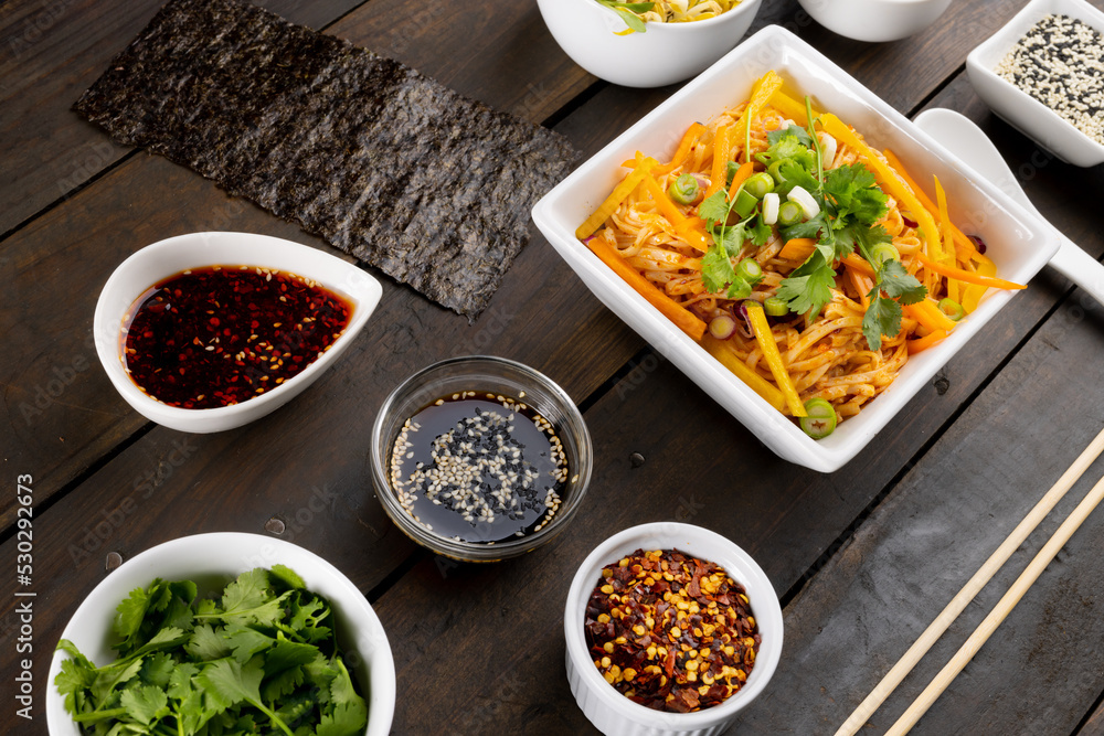 Overhead view of asian wok stir fry noodles with chopsticks and condiments on wood