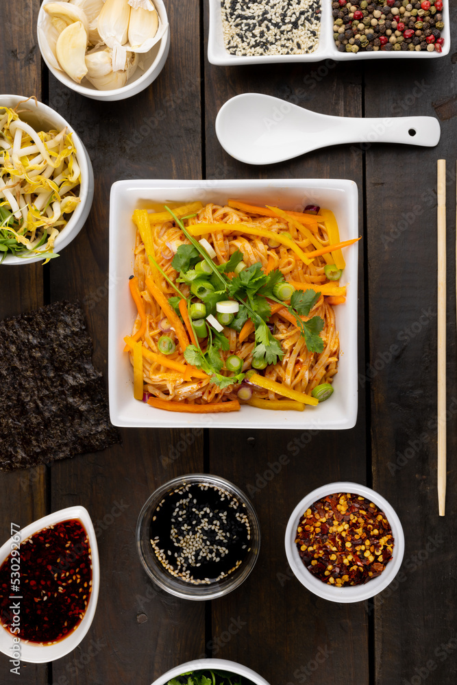 Overhead view of asian wok stir fry noodles with chopsticks, spoon and condiments on wood