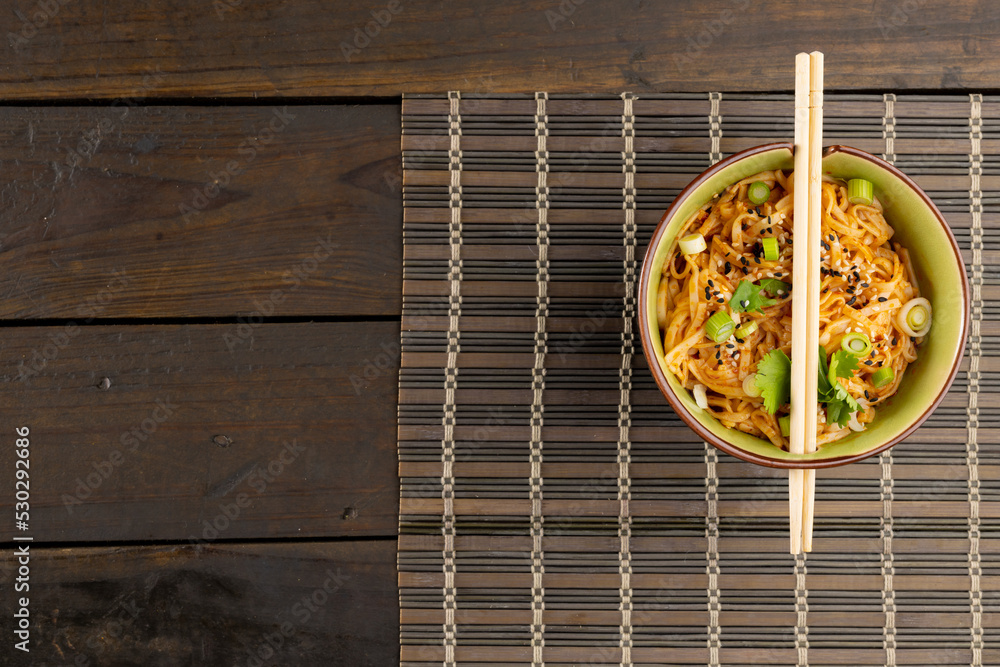 Overhead view of asian wok stir fry noodles with chopsticks on mat and wooden boards