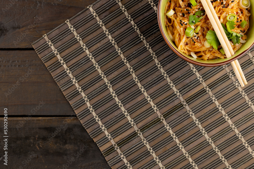 Overhead view of asian wok stir fry noodles with chopsticks on mat and wooden boards