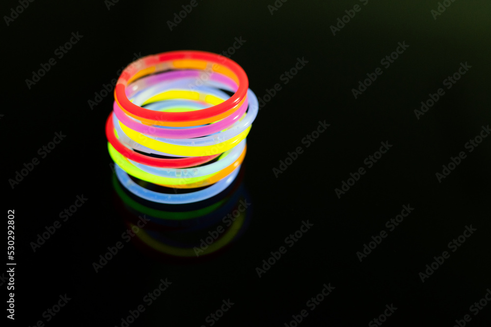 Image of vibrant round neon glow sticks stacked over black background with copy space