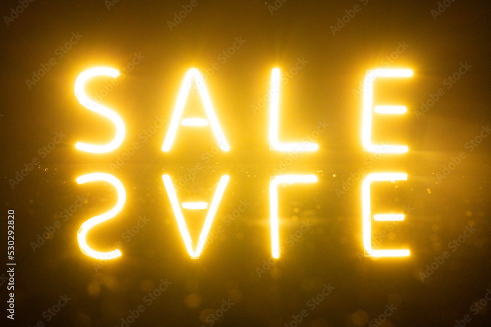 Image of glowing neon sale text with reflection over orange background