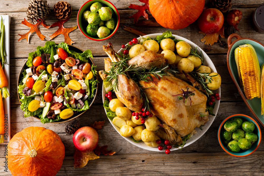 Overhead view of thanksgiving table with roast turkey, vegetables and autumn decoration on wood