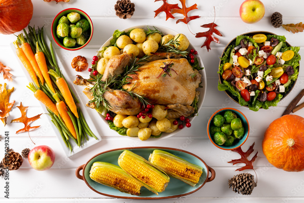 Overhead view of thanksgiving table with roast turkey, vegetables and autumn decoration on wood