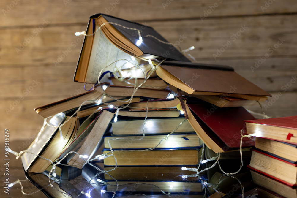 Image of christmas decoration with fairy lights and stack of books on wooden background