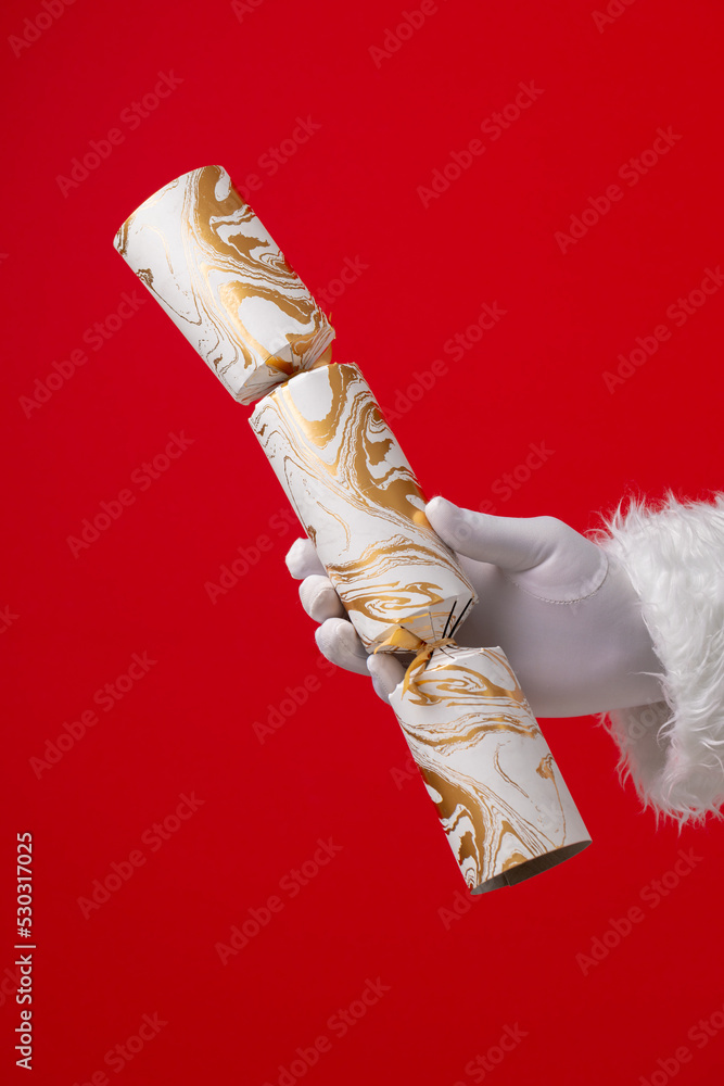 Image of hand of santa claus holding christmas cracker with copy space on red background