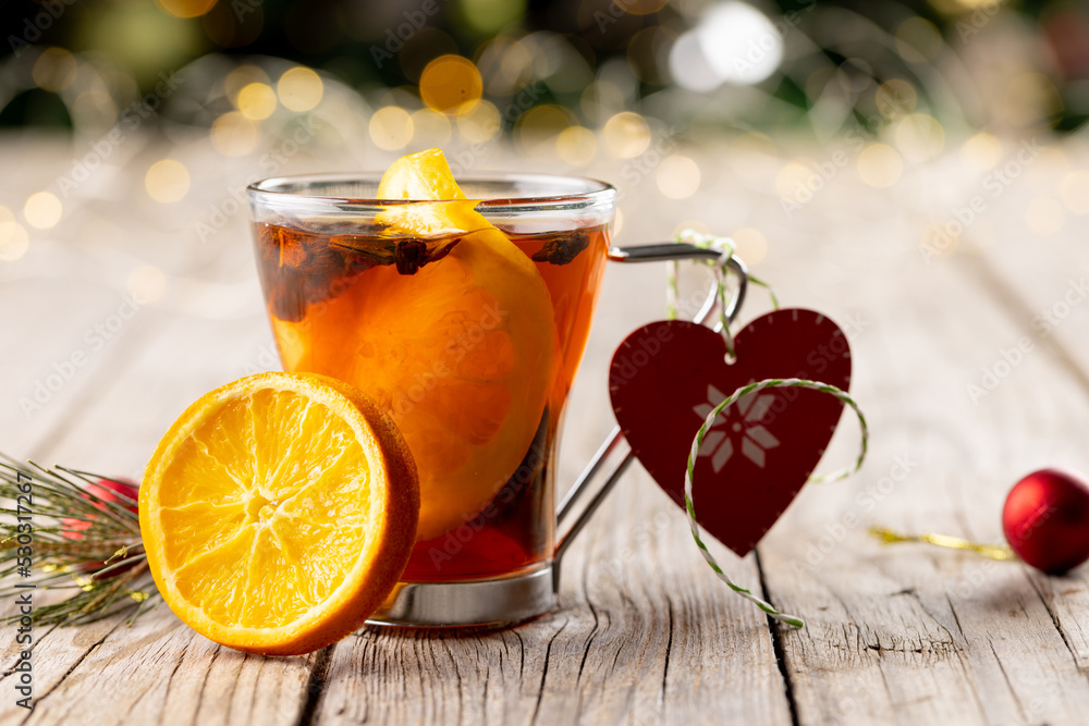 Image of cup of tea with spices and lemon and christmas decorations on wooden backgorund