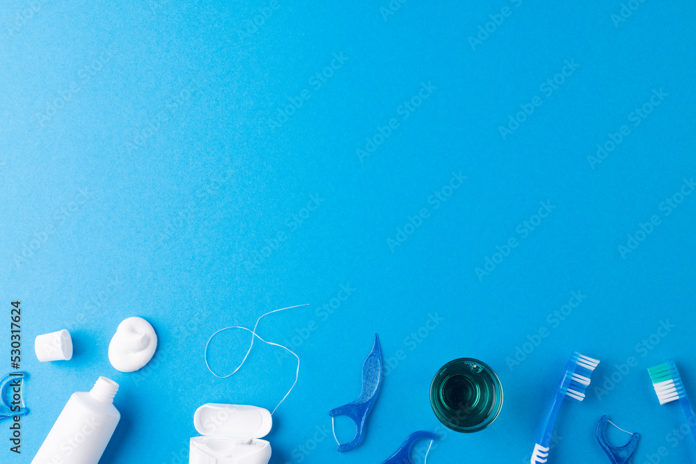 Image of toothbrush, toothpaste, string and liquid on blue surface