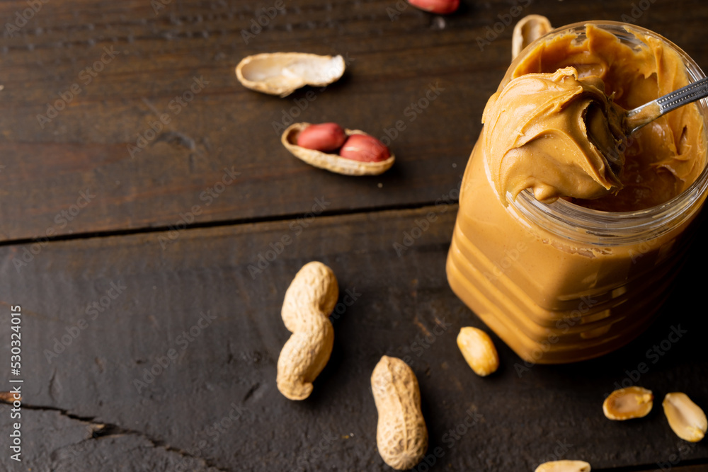 Image of jar with peanut butter and nuts on wooden surface