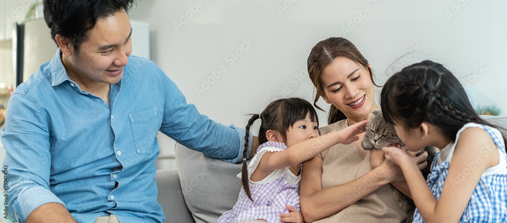 一对亚洲情侣和年幼的女儿在客厅抚摸一只猫。