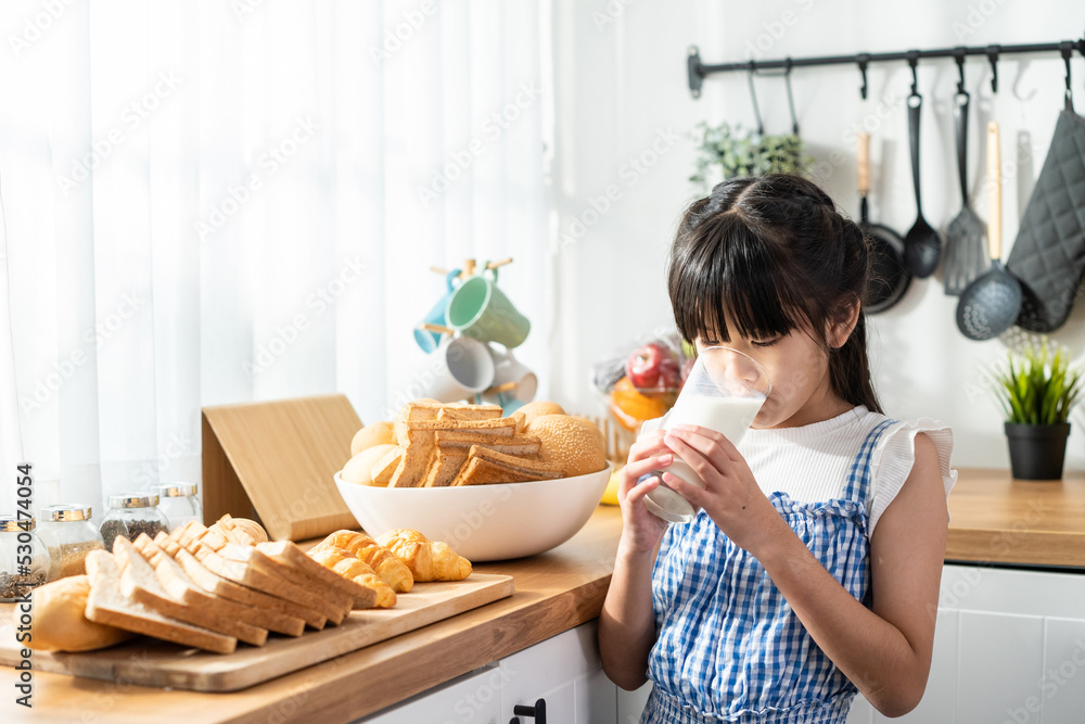 亚洲小孩拿着一杯牛奶在家里的厨房里喝水