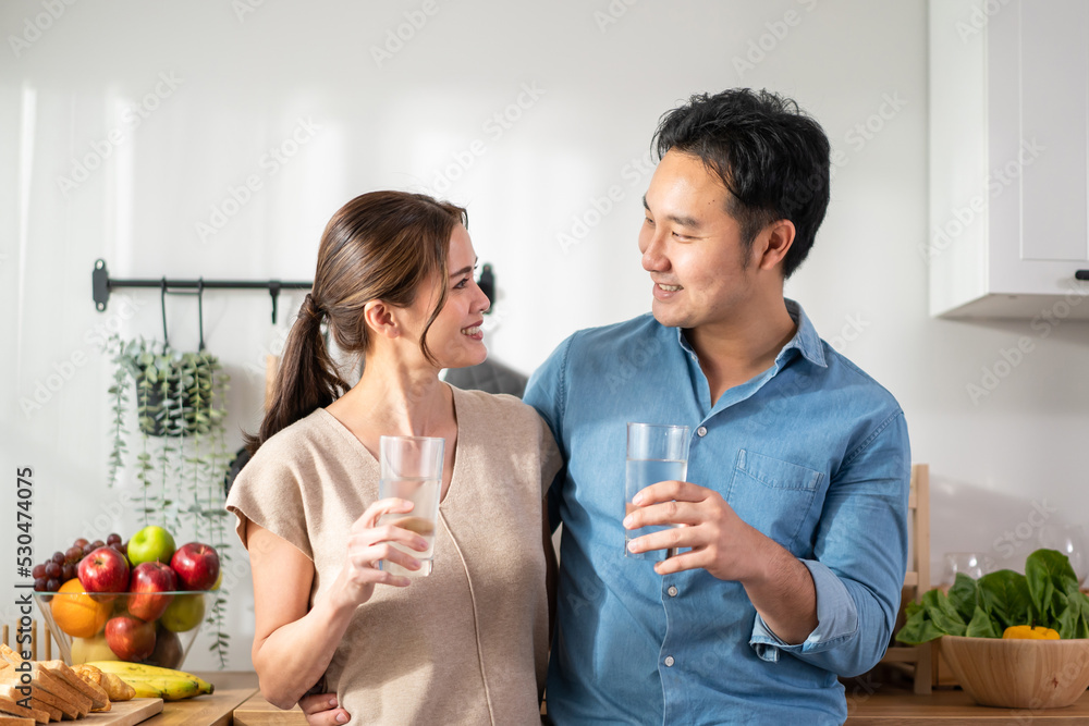 Asian attractive couple drinking a glass of water in kitchen at home. 