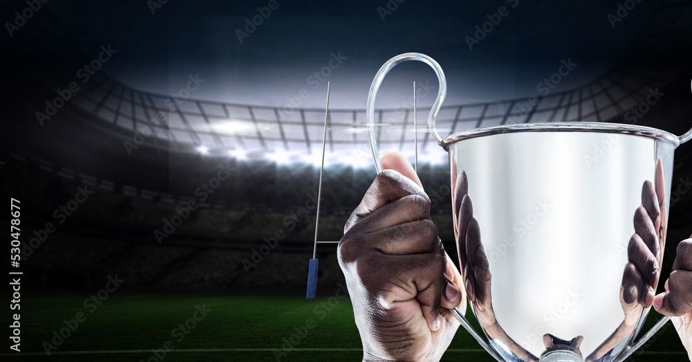 Composition of male rugby player celebrating victory, holding trophy on rugby pitch at stadium