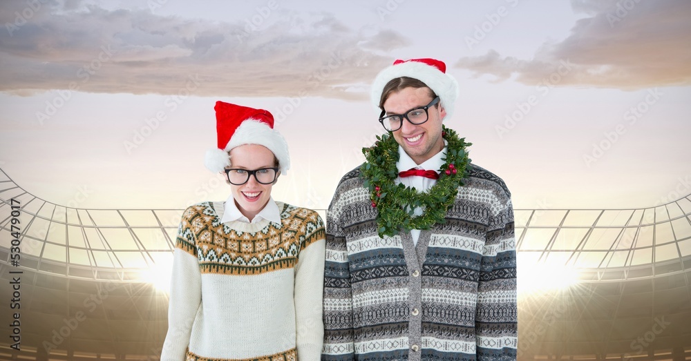 Composite image of caucasian couple wearing santa hats against sports stadium with copy space