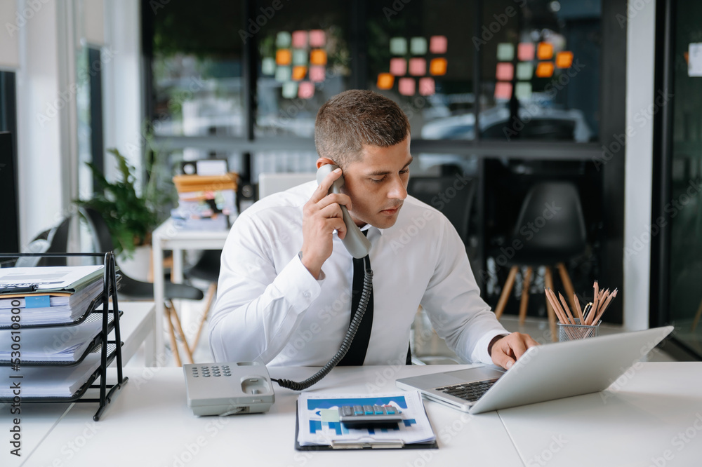 Businessman Talking on the phone and using a laptop with a smile while sitting at office