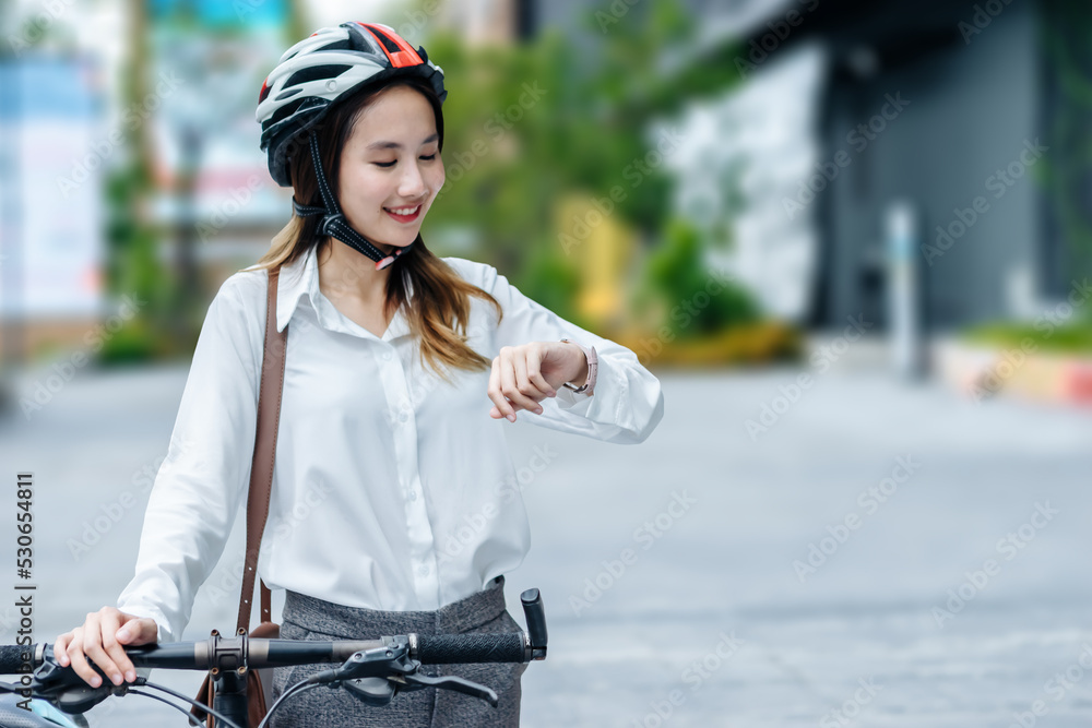 年轻的亚洲女商人戴着头盔，骑着自行车站在城市街道上看天空