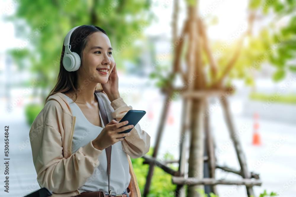 美丽的亚洲女人用手机耳机听最喜欢的音乐，幸福放松