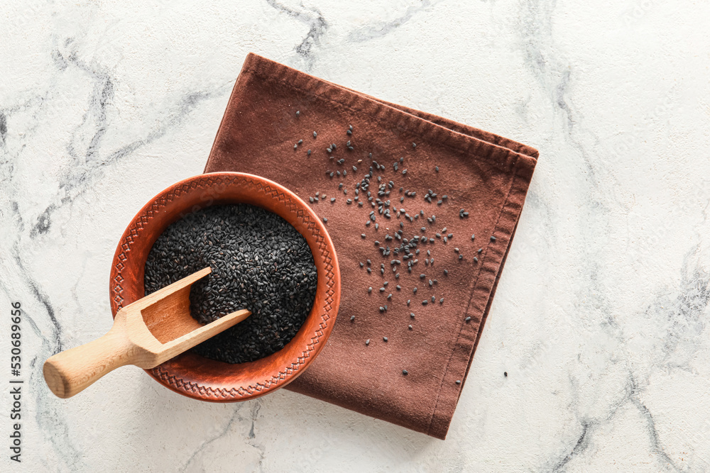 Bowl and scoop of black sesame seeds on light background