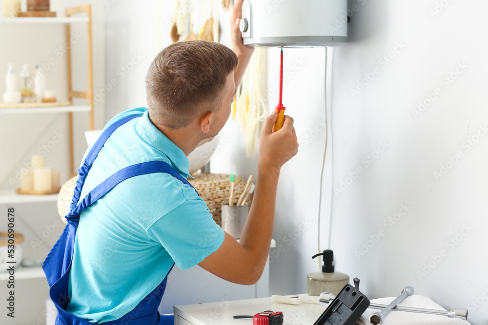 Male plumber repairing boiler with screwdriver in bathroom