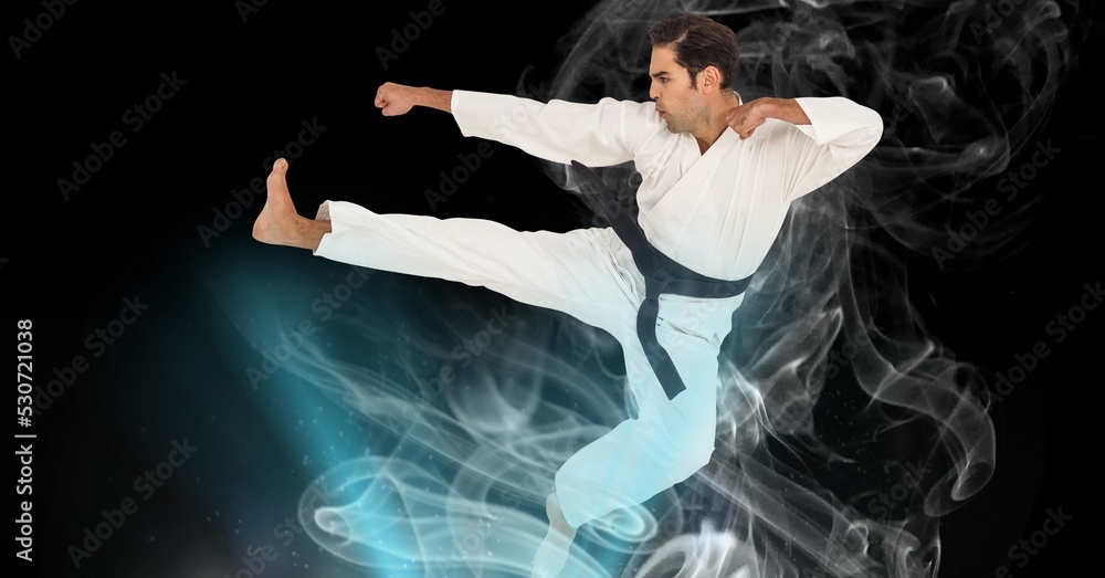 Composition of male martial artist over trails of smoke on black background