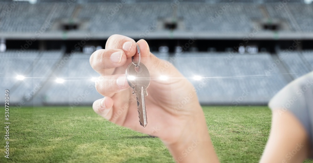 Composition of businesswoman holding key over sports stadium