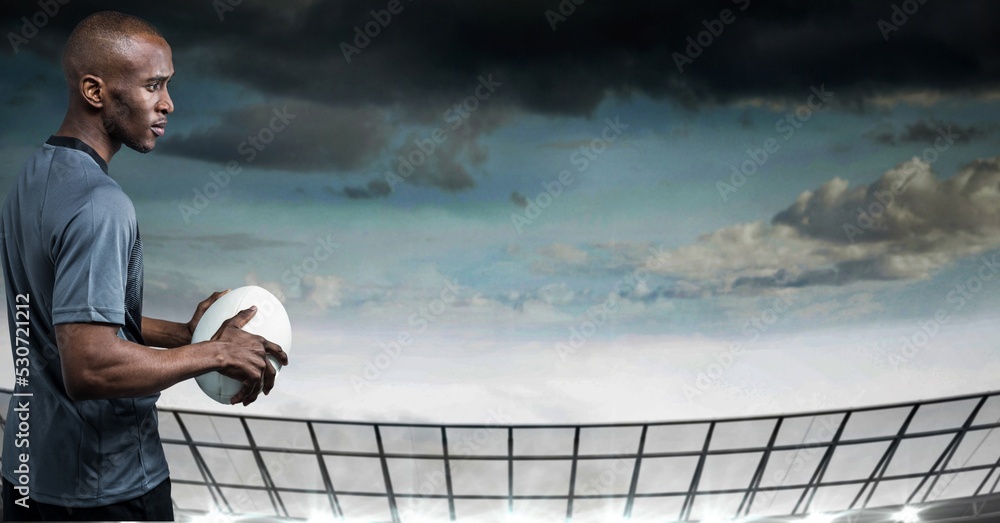 Composition of male rugby player holding rugby ball over sports stadium