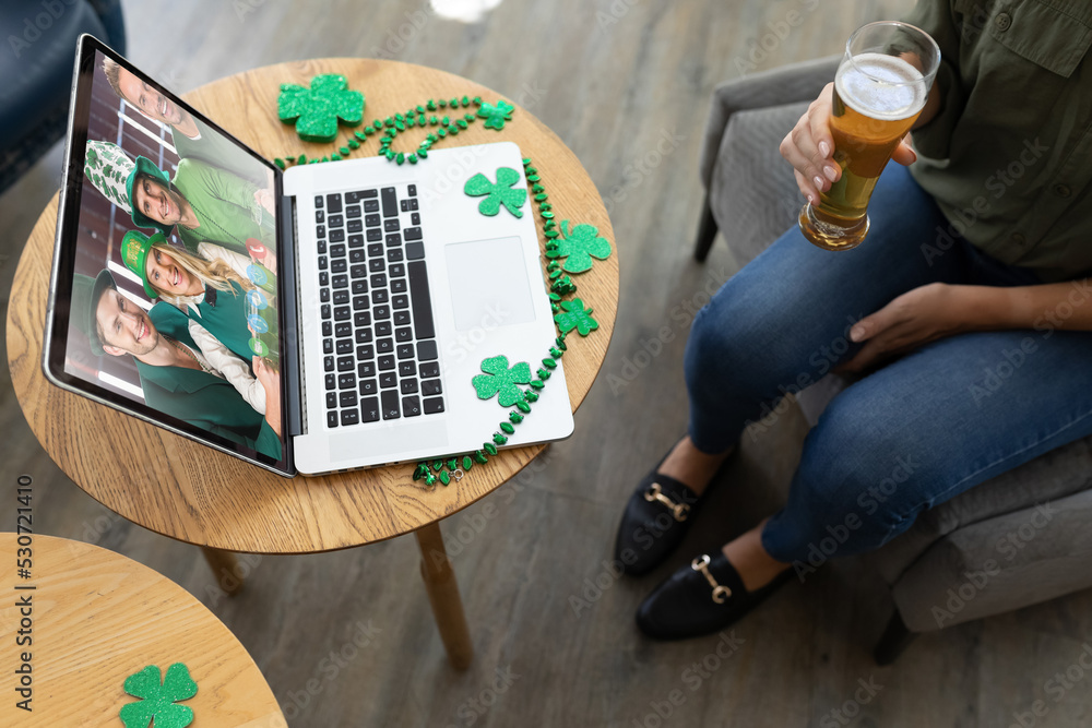 Caucasian woman at bar holding beer making st patricks day video call to friends on laptop