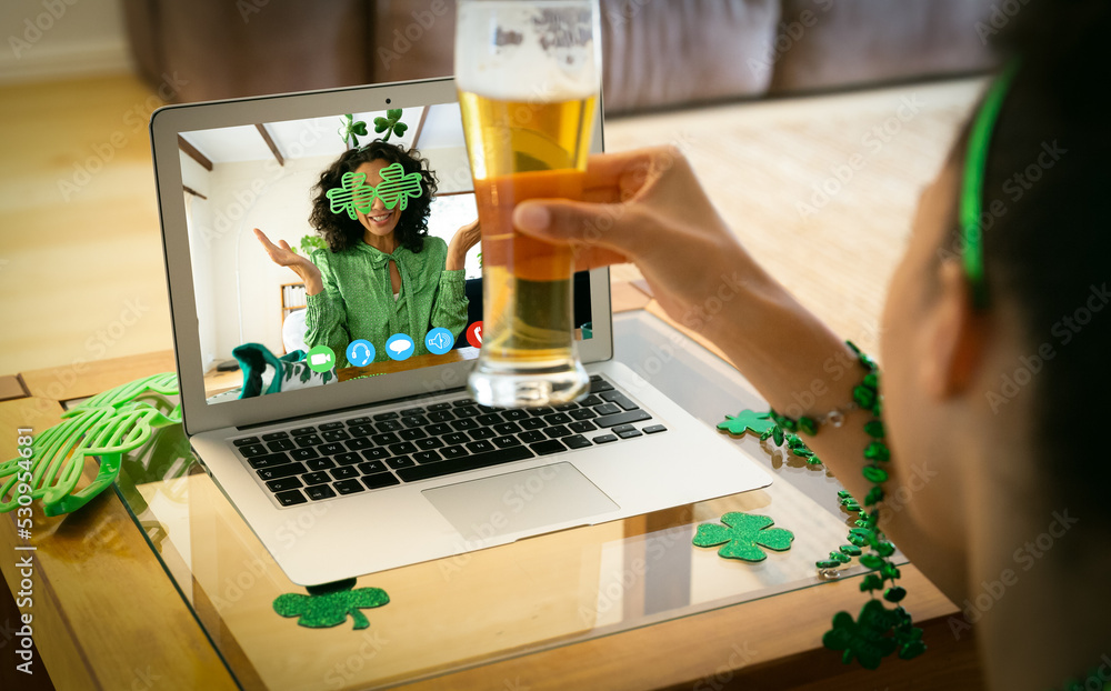 African american woman holding a beer glass having a video call on laptop at home