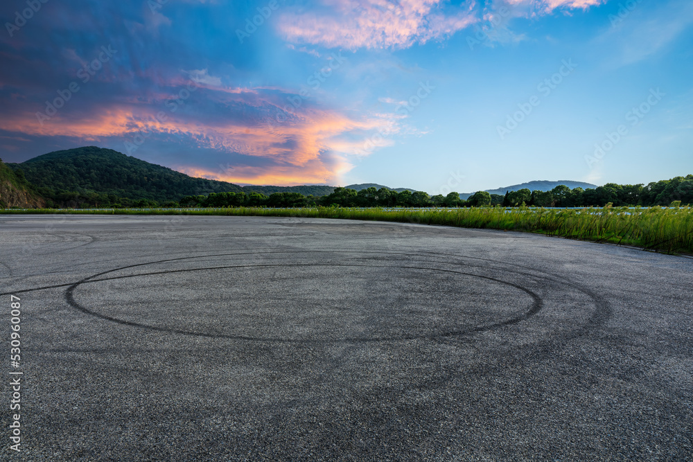 空旷的沥青赛道道路和日出时天空乌云密布的山峰