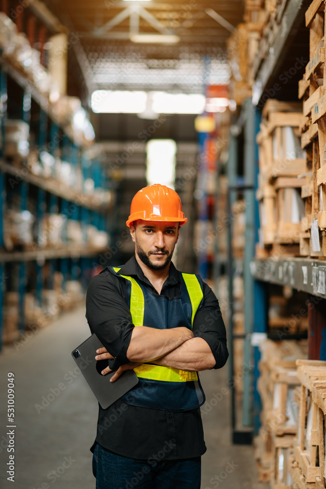 Male factory manager using digital tablet in warehouse shelf looking at camera.Products and corrugat