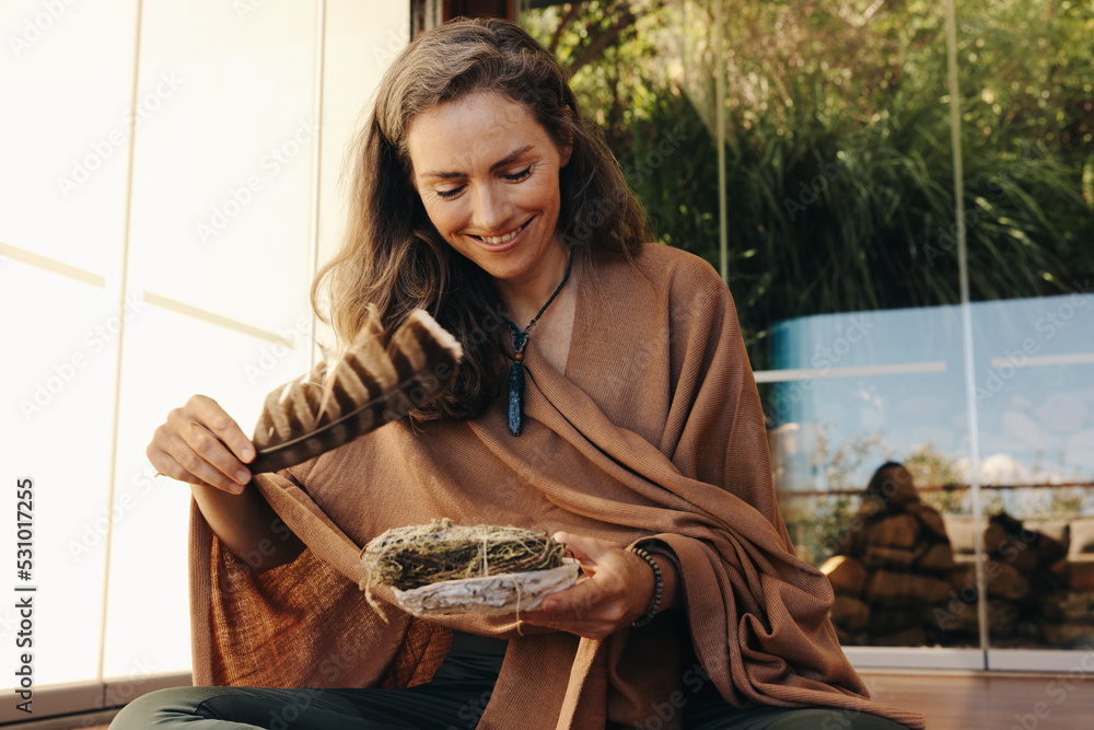 拿着一根鼠尾草涂抹棒和一根羽毛的快乐高级女性