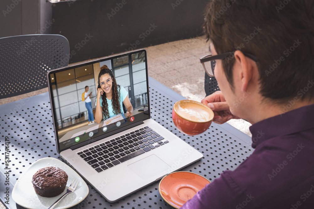 Multiracial businessman discussing with coworker on videocall over laptop while drinking coffee