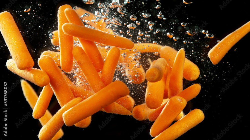 Baby carrots pieces splashing underwater.