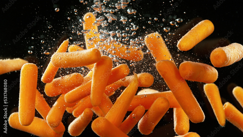 Baby carrots pieces splashing underwater.