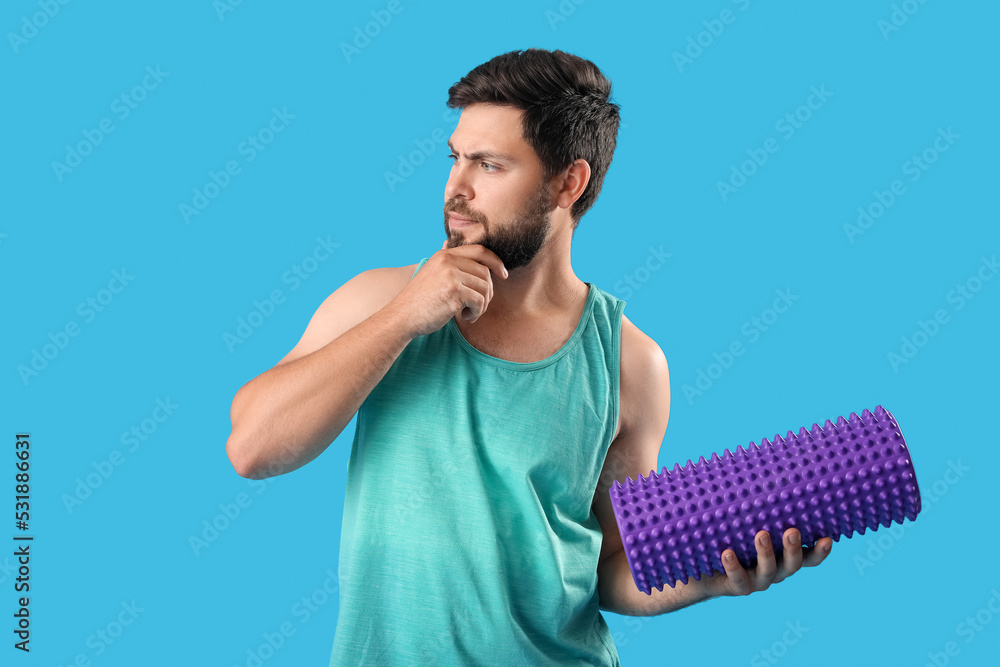 Thoughtful young man with foam roller on blue background