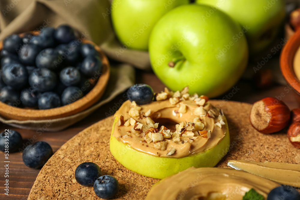 Cork mat of tasty apple rounds with nut butter on wooden table, closeup