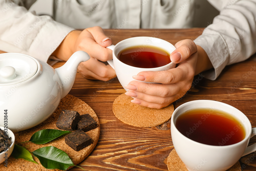 Female hands with cups of hot puer tea on wooden background, closeup