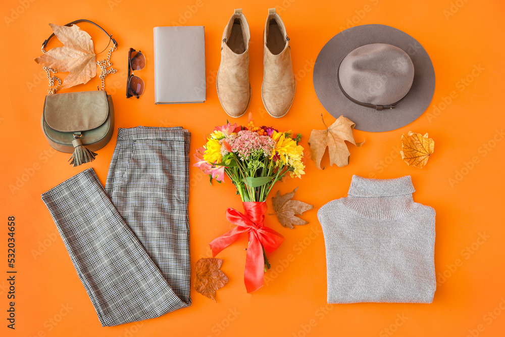 Stylish female accessories, bouquet of flowers and autumn leaves on orange background