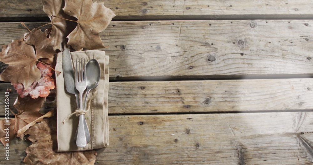 Image of light spots over cutlery and leaves on wooden background