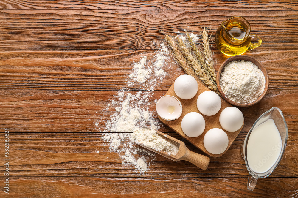 Ingredients for baking and wheat ears on wooden background