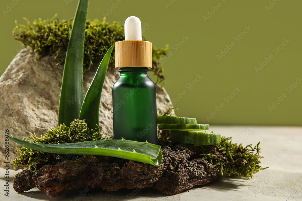 Composition with bottle of essential oil, aloe vera leaves and tree bark on table against green back