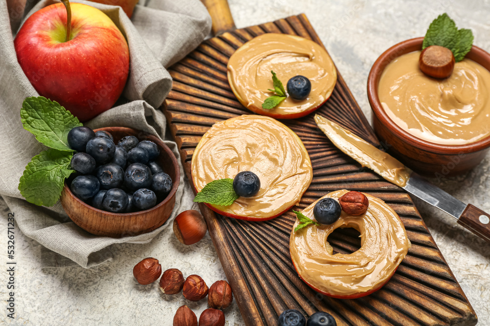 Wooden board of tasty apple rounds with nut butter and blueberry on light background, closeup