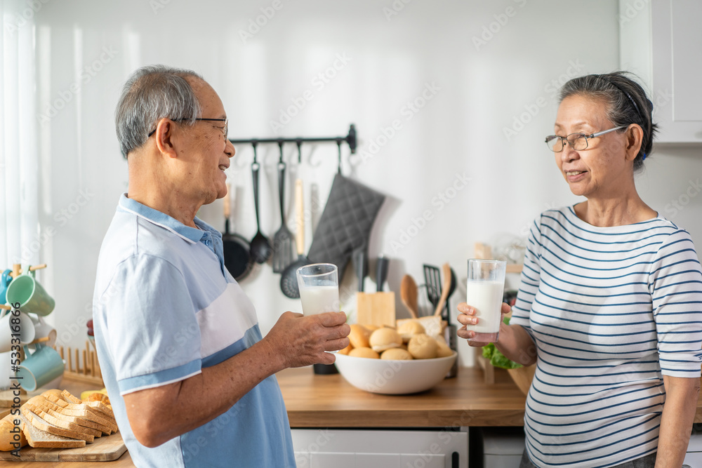 亚洲一对老年夫妇在家里的厨房里喝了一杯牛奶。